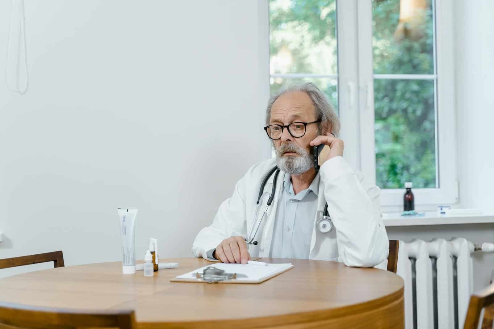 a man in a white coat with a stethoscope on his neck talking on a phone